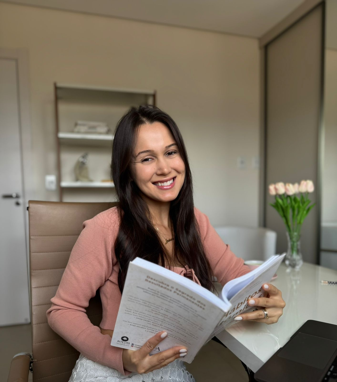 Andressa Guimarães em seu ambiente de trabalho, segurando um livro